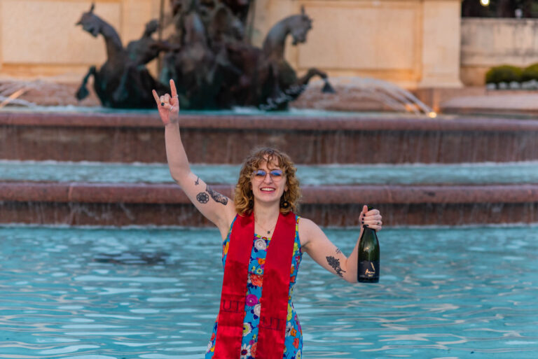 girl posing in the fountain at the university of texas raising arm in hook em horns sign