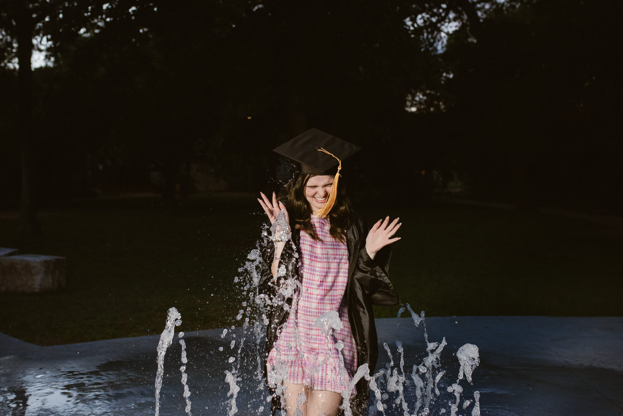 girl with cap and gown running through splash pad for her senior photos