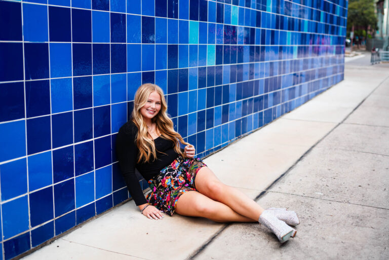 girl sitting by unique blue wall for senior photos