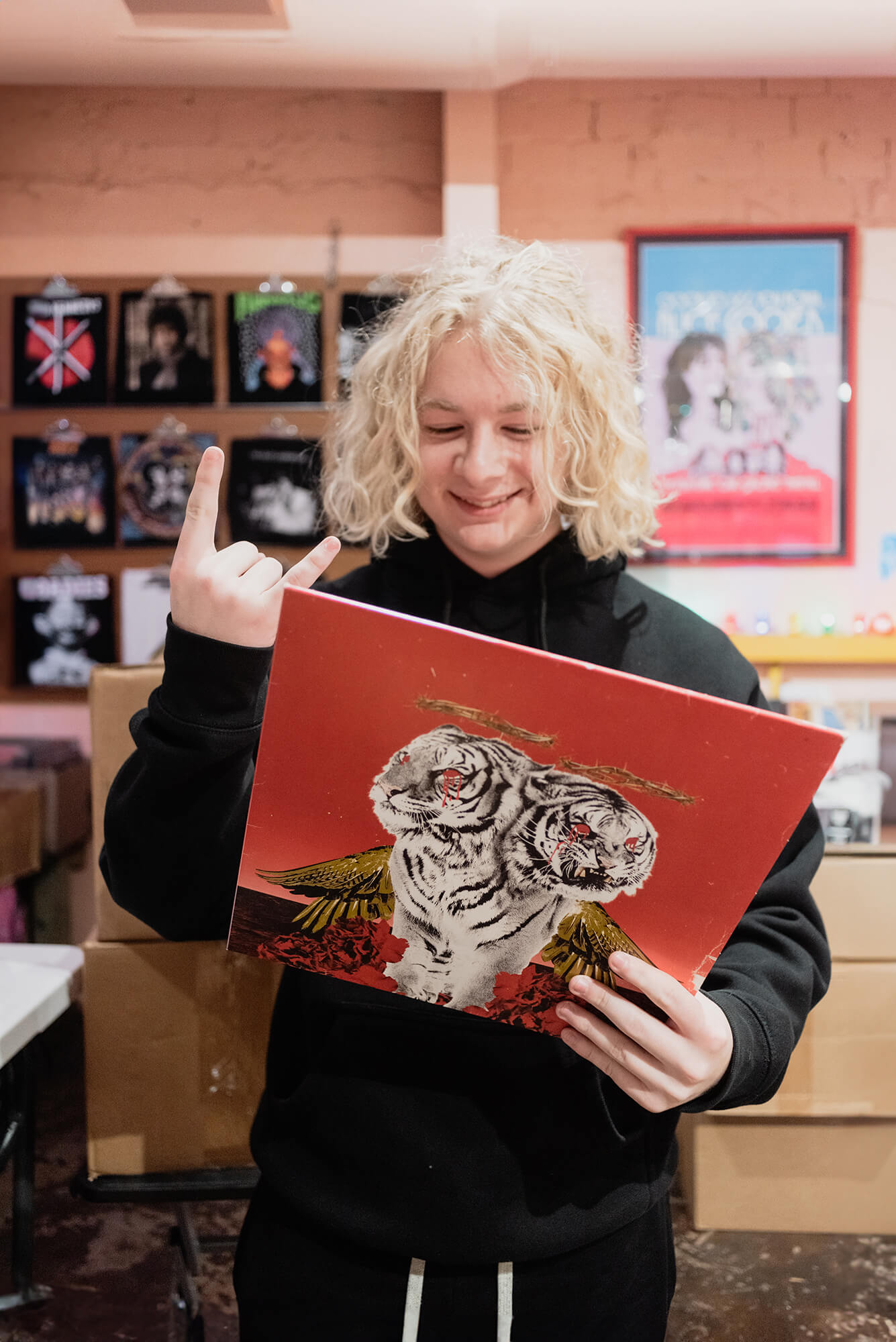 senior holding one of his favorite records in one hand showing the rock and roll hand sign in his other hand for his senior photos at a record store in dallas texas