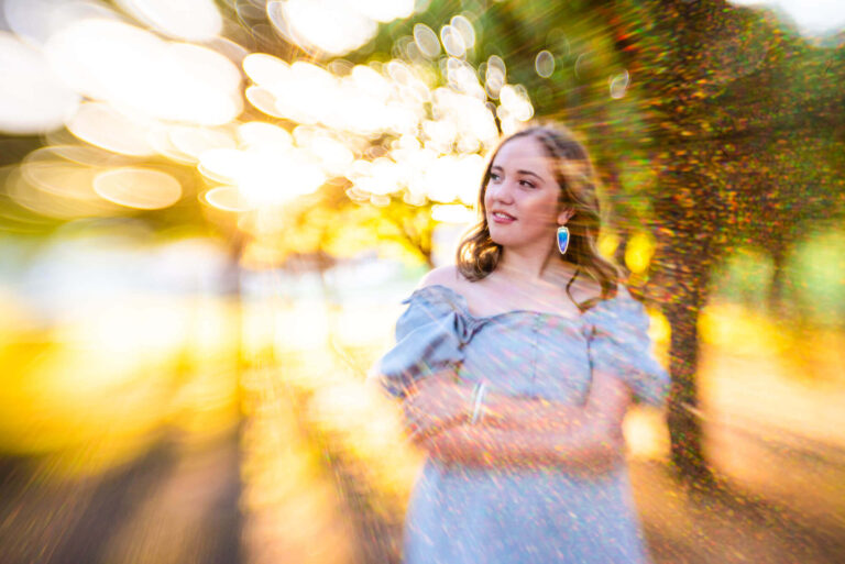 teen girl smiling, hugging herself looking away for portraits. lots of sun and colorful light reflected