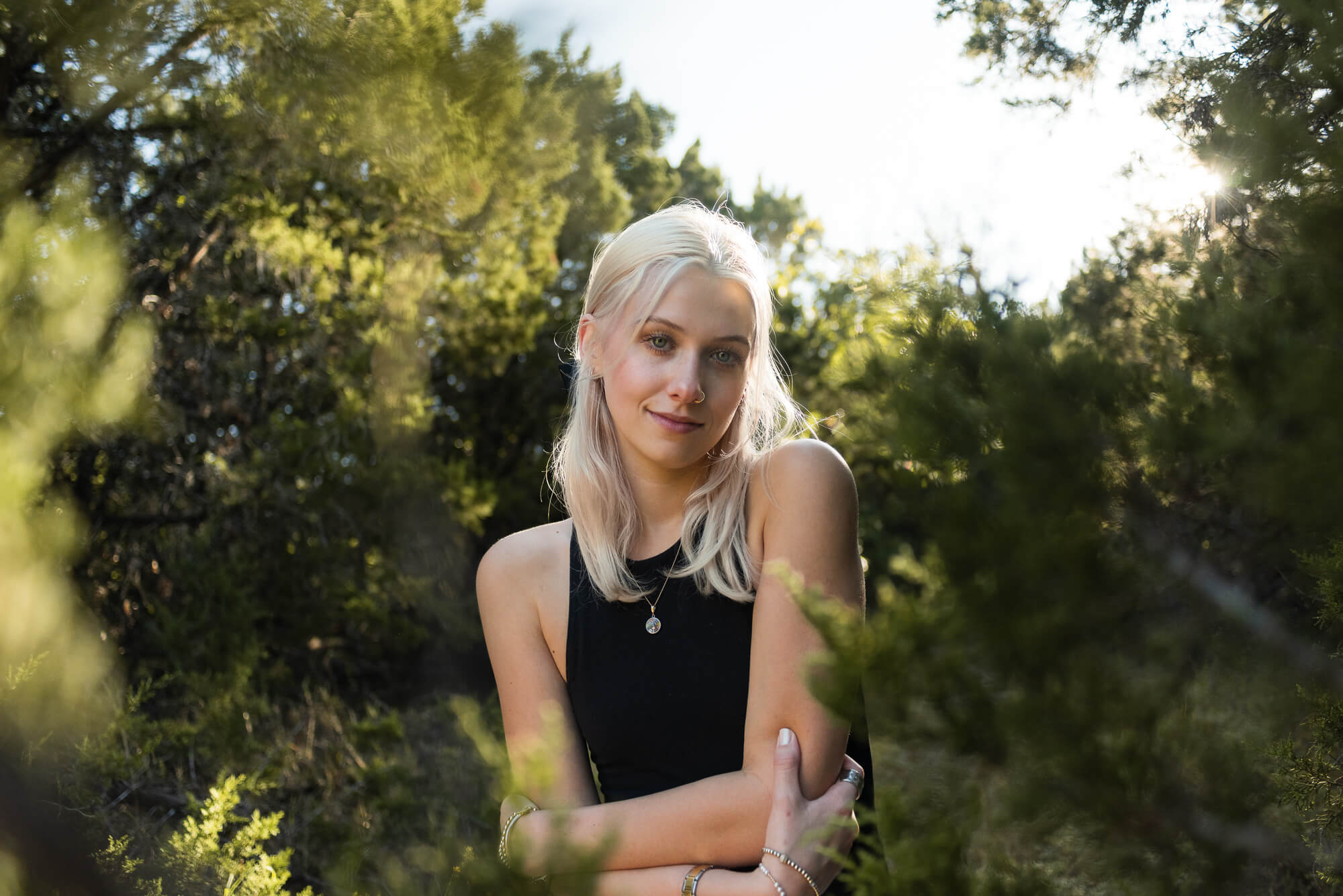 girl surrounded by evergreen tree branches with a slight smile at the camera during her senior photos in austin texas