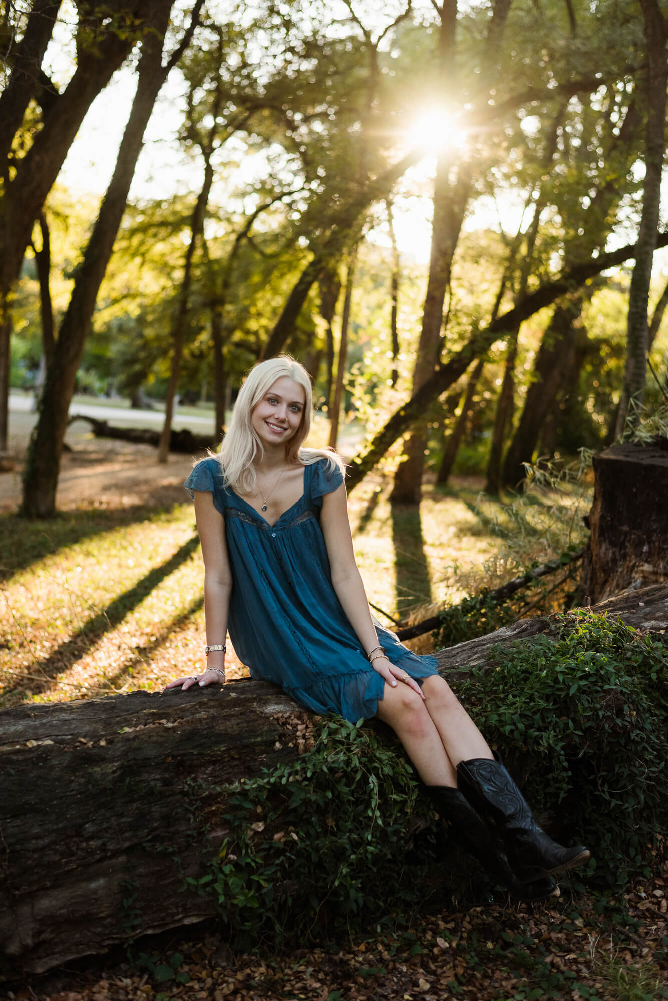 girl sitting on fallen tree and smiling at camera for senior portraits