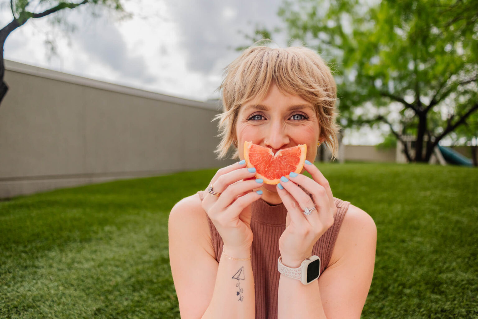 woman holding orange slice up to her face like it's her smile