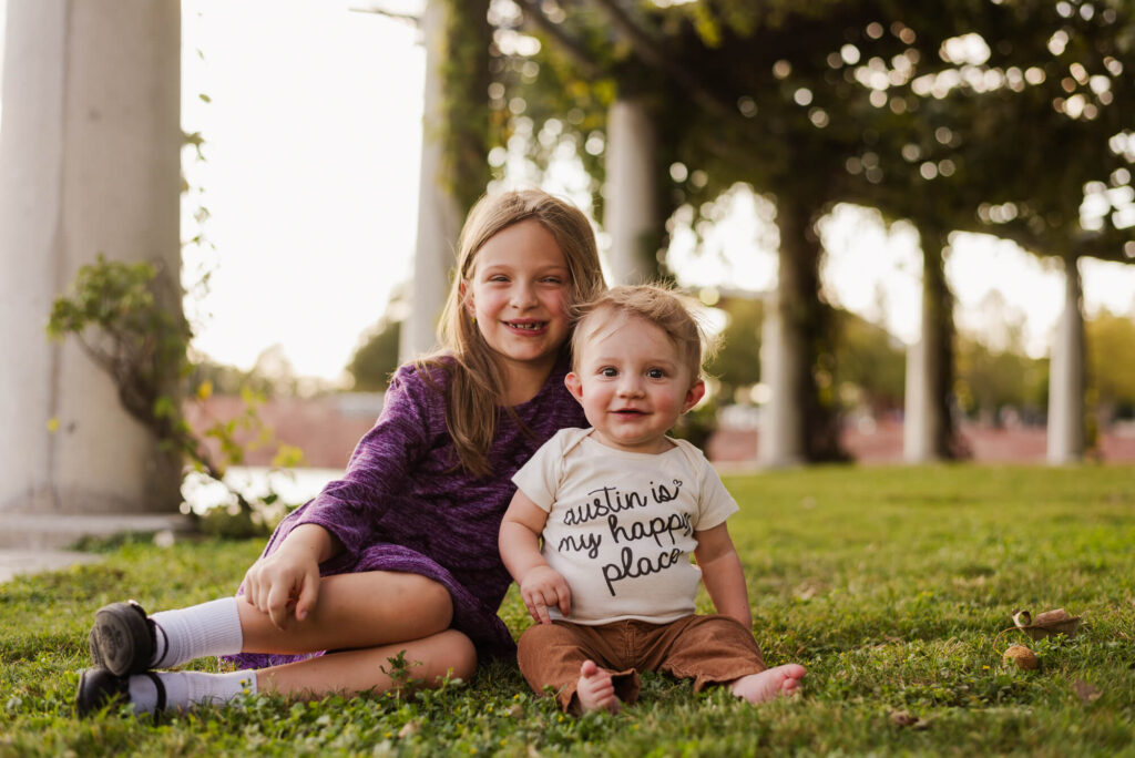 Sister and brother sitting on the grass during sibling milestone photoshoot