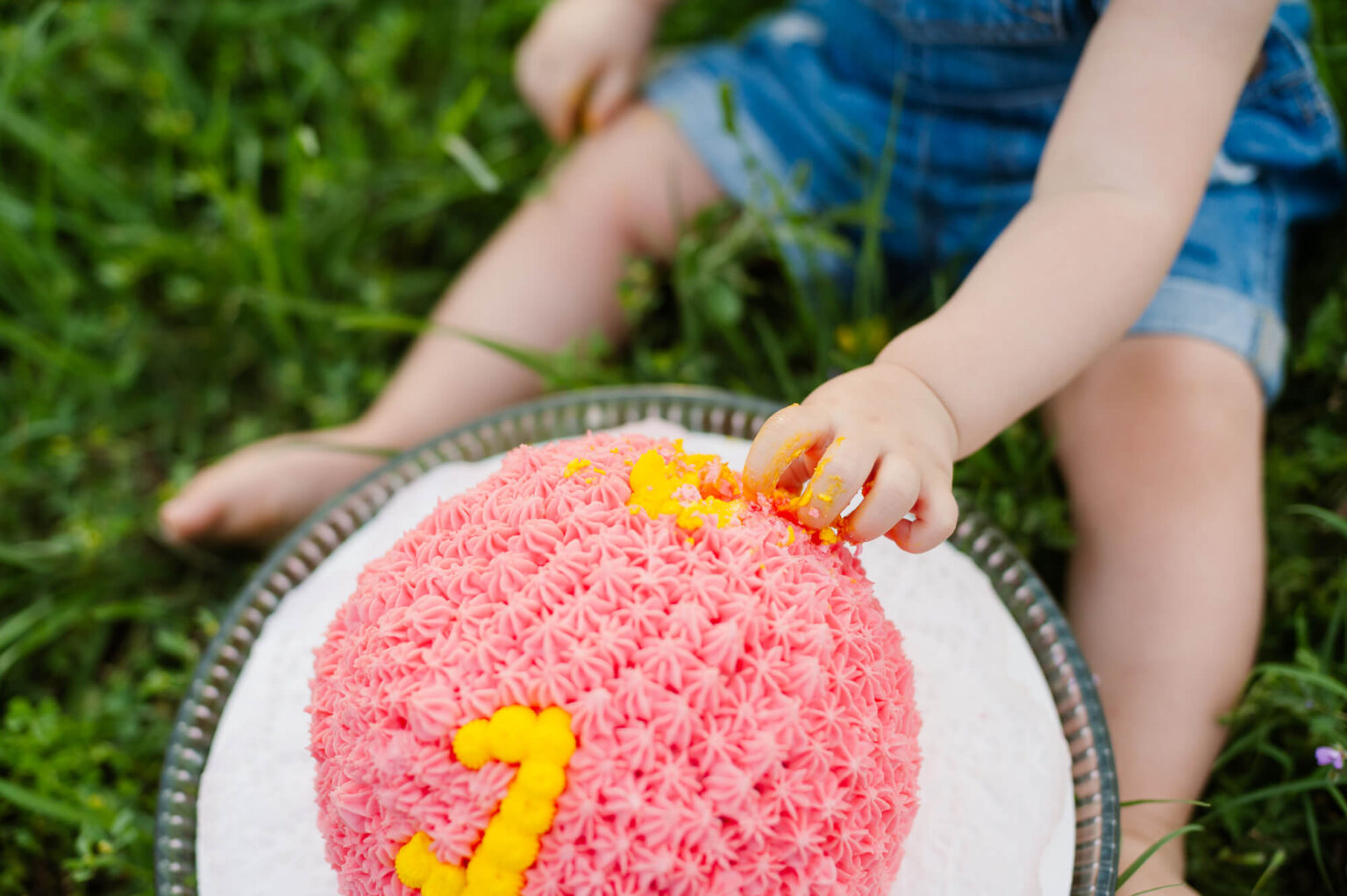 one year old girl playing with cake icing during her first birthday cake smash photoshoot