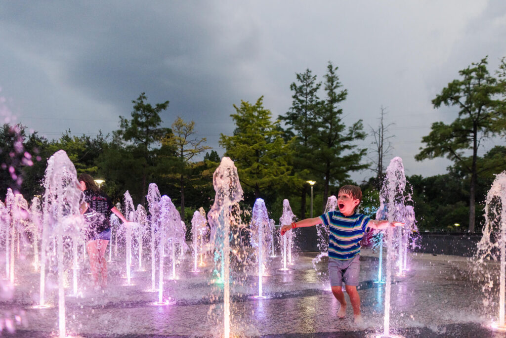 boy running through colorfully lit splashpad at liz carpenter fountain in austin texas