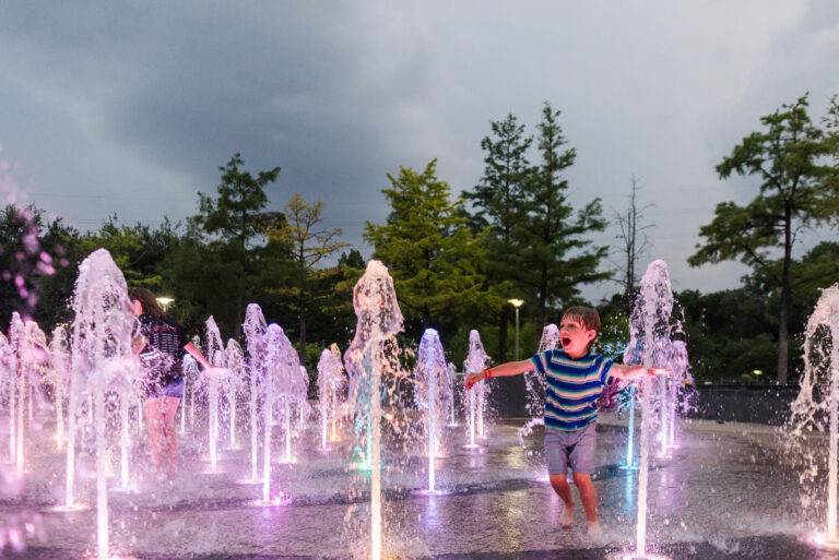 boy running through colorfully lit splashpad at liz carpenter fountain in austin texas