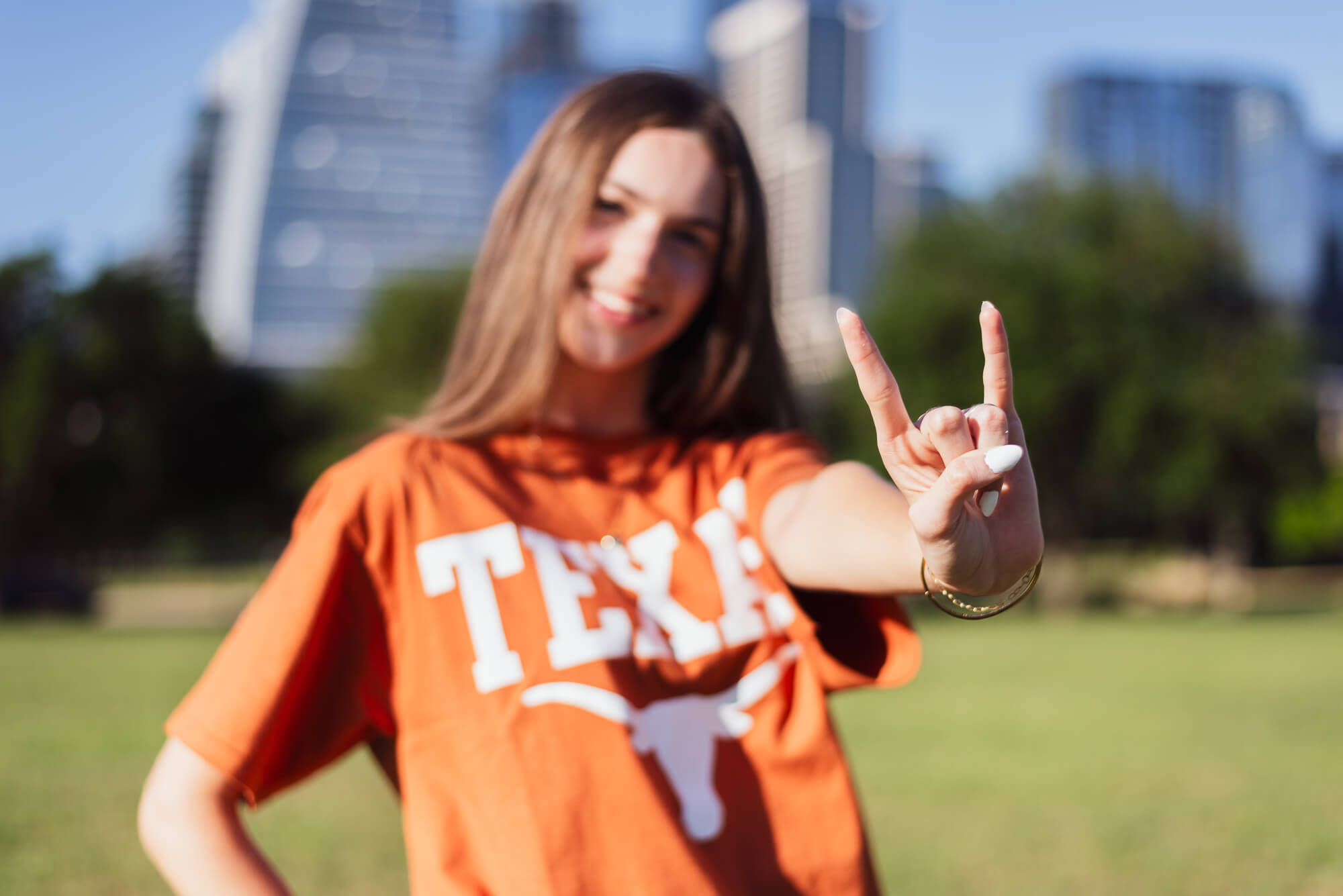high school senior girl in front of the skyline with her hands in the hook 'em horns for ut
