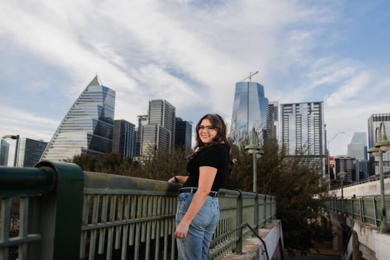 girl standing on pedestrian bridge during senior photoshoot with austin skyline in the background