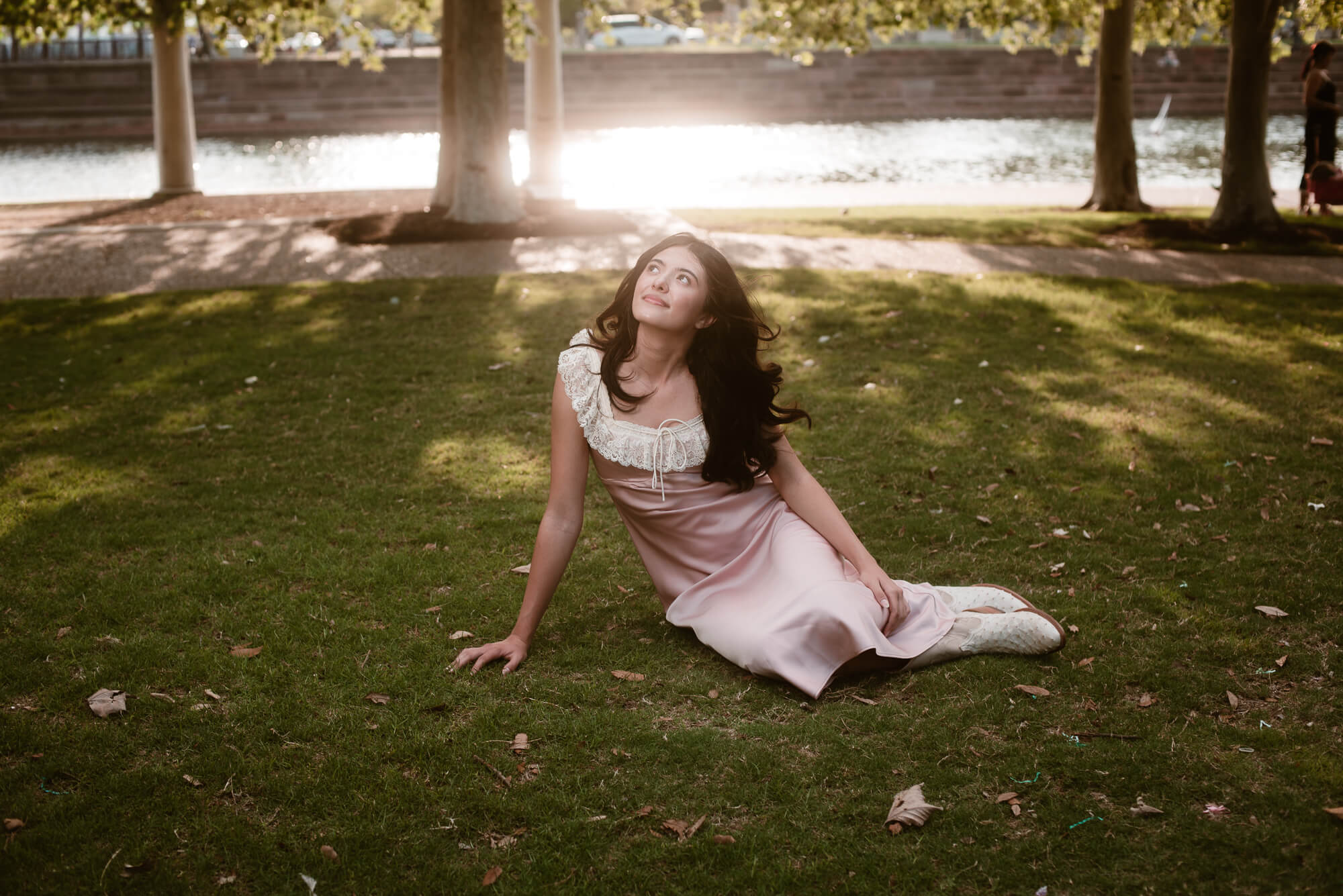 soft dreamy senior photo of girl sitting on ground at mueller lake park gazing off into the distance