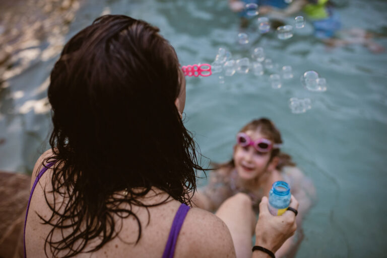 mom blowing bubbles while kiddo is swimming in pool