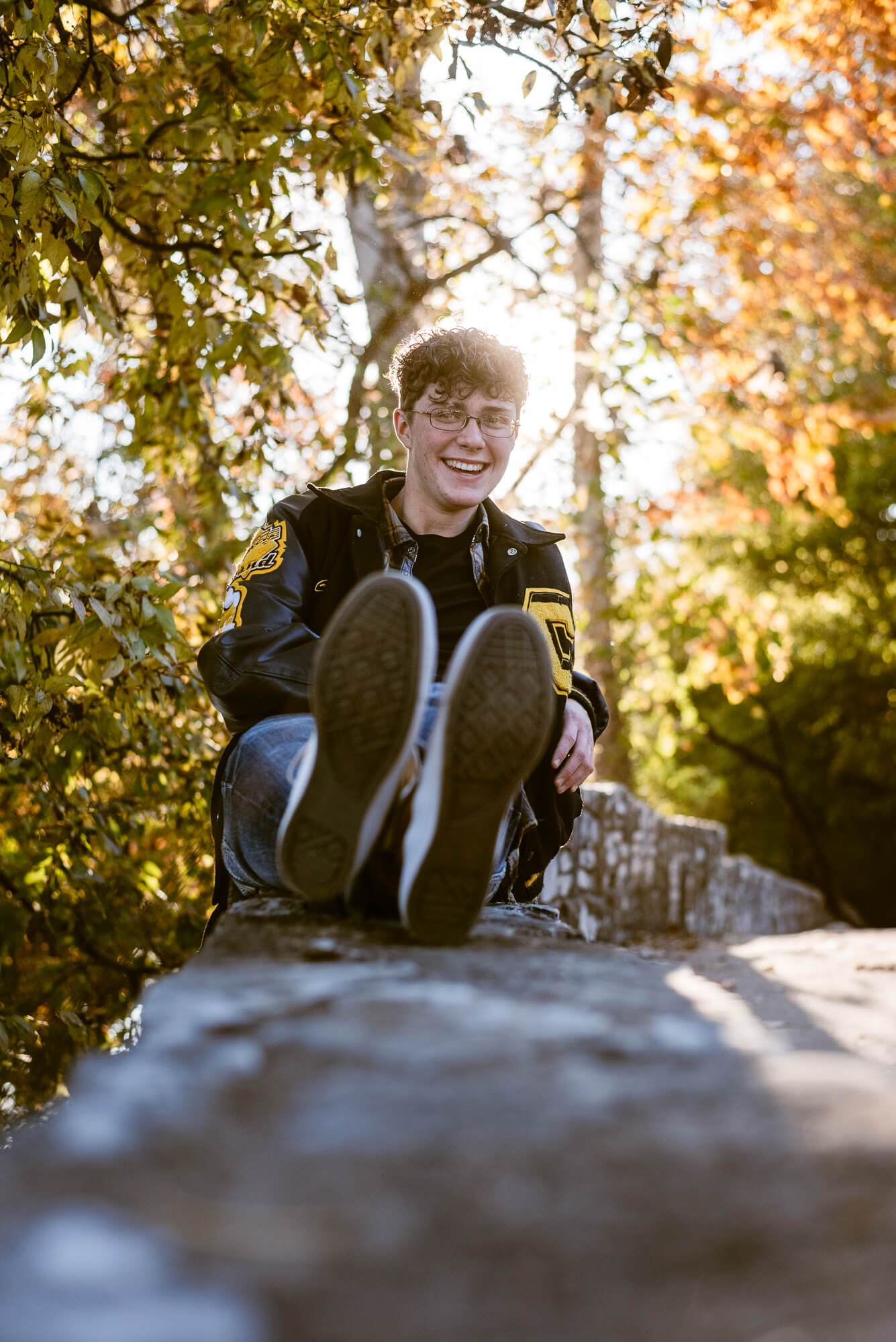 boy laughing during senior photoshoot with fall tree colors in background