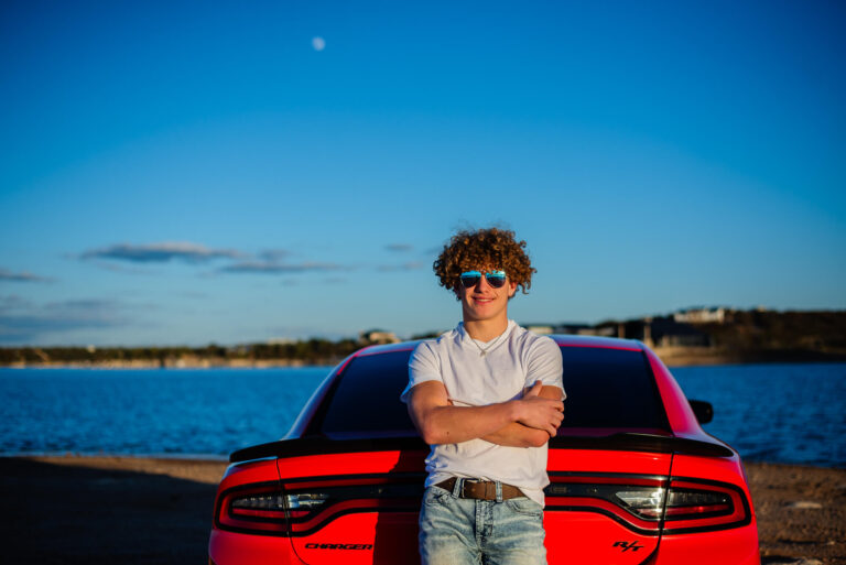 senior guy leading against his red sports car at the lake for his senior photos