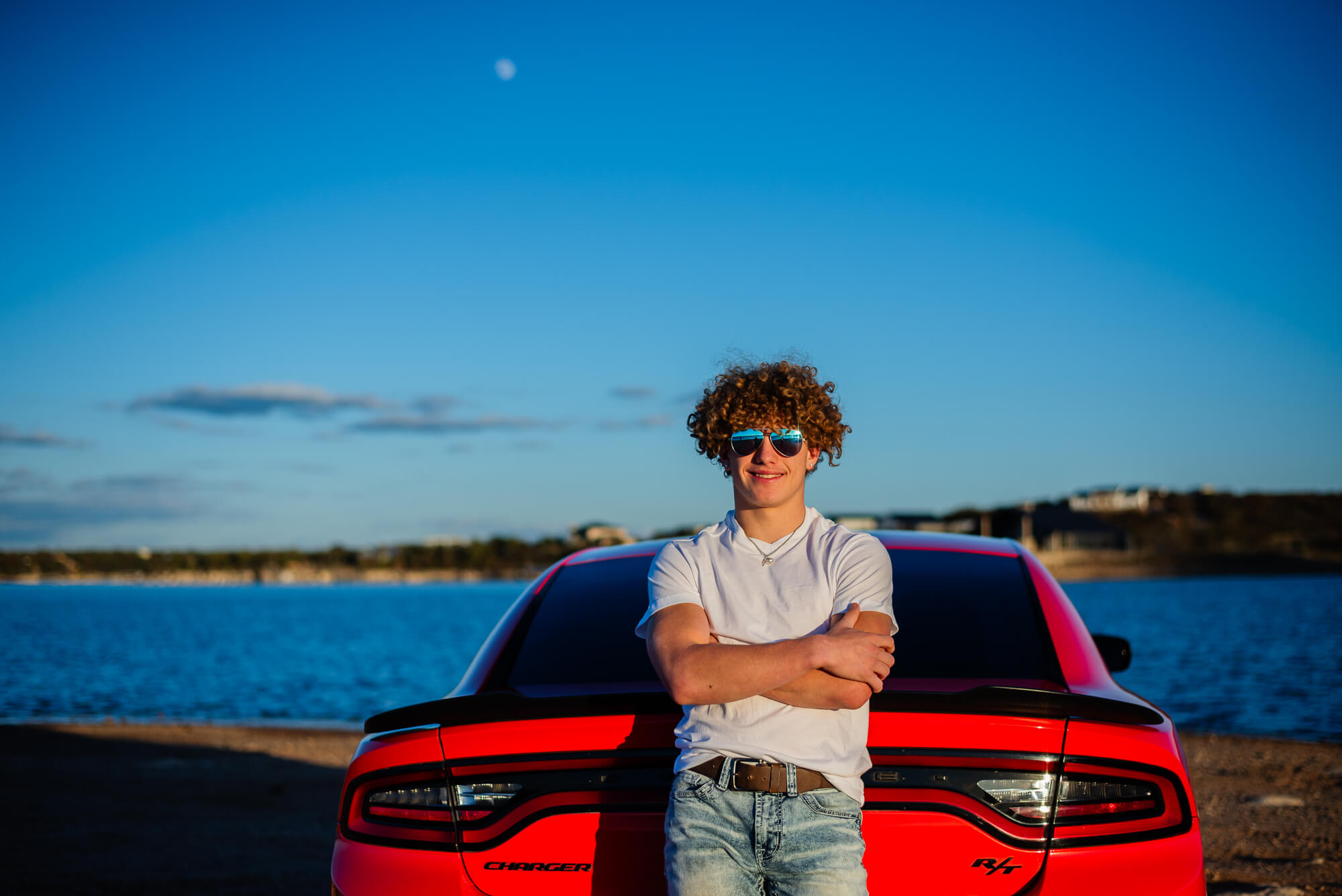 senior guy leading against his red sports car at the lake for his senior photos