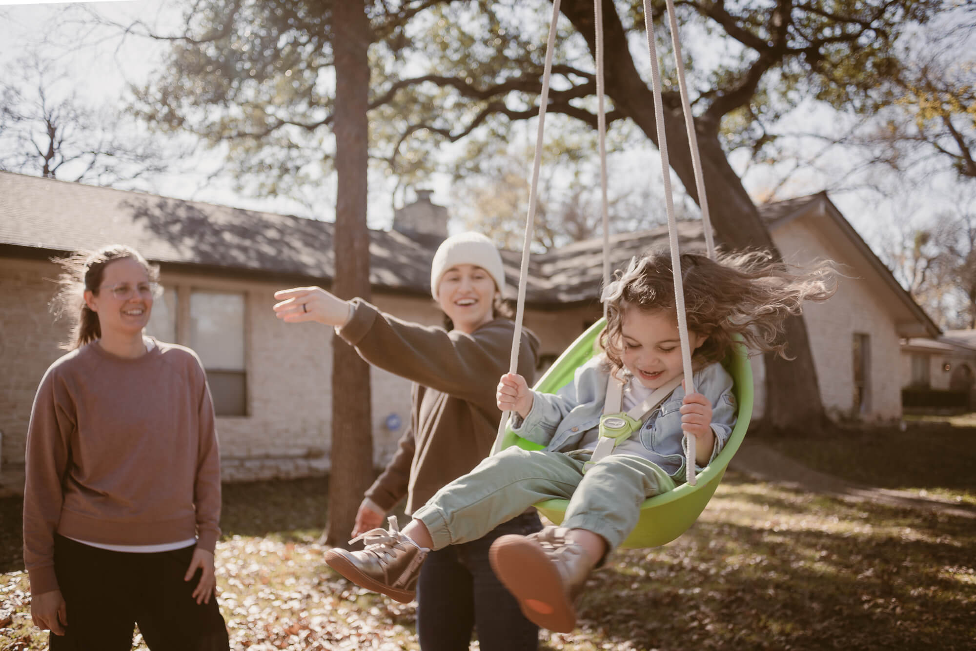 Parent pushing their toddler on the swing in the front yard during an at-home family photoshoot