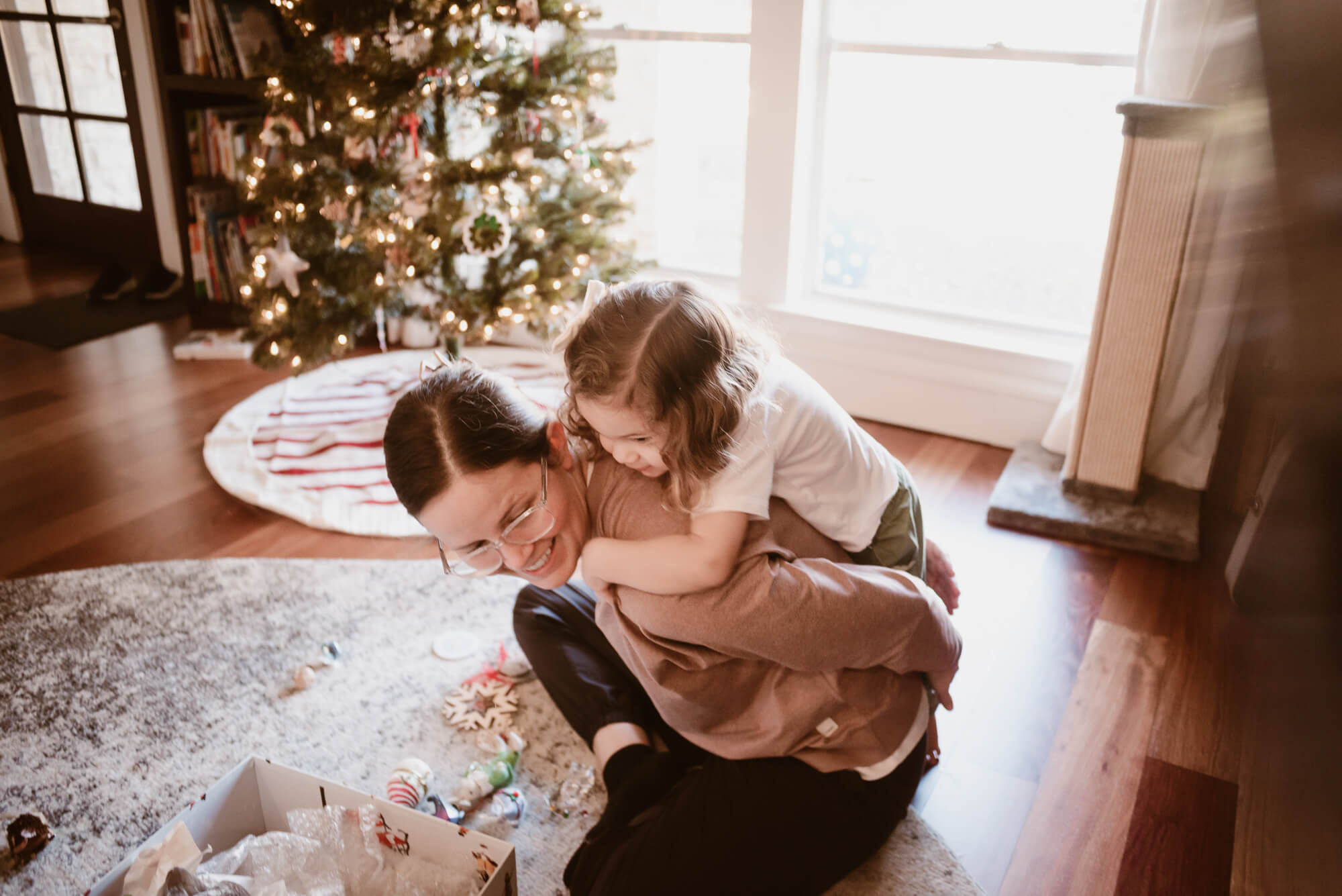 Candid moment of a toddler with their parents by the Christmas tree at home