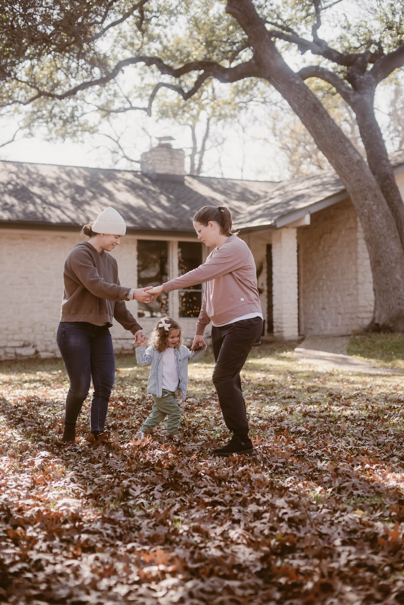 Candid moment of a family playing ring around the rosie in the leaves outside their home in Austin
