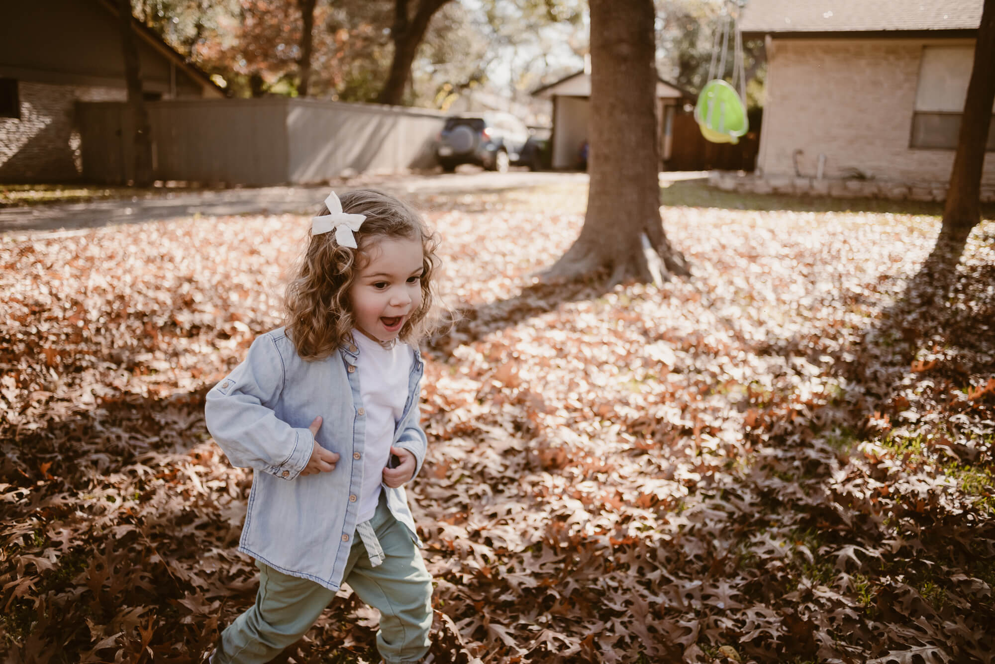 toddler playing outside in the front yard in leaves during an at home family photoshoot in austin texas