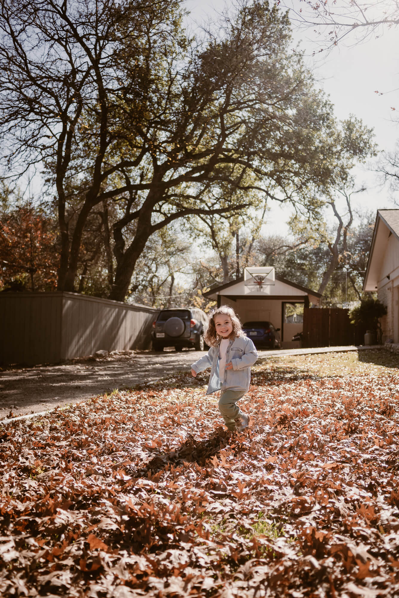 toddler playing outside in the front yard in leaves during an at home family photoshoot in austin texas