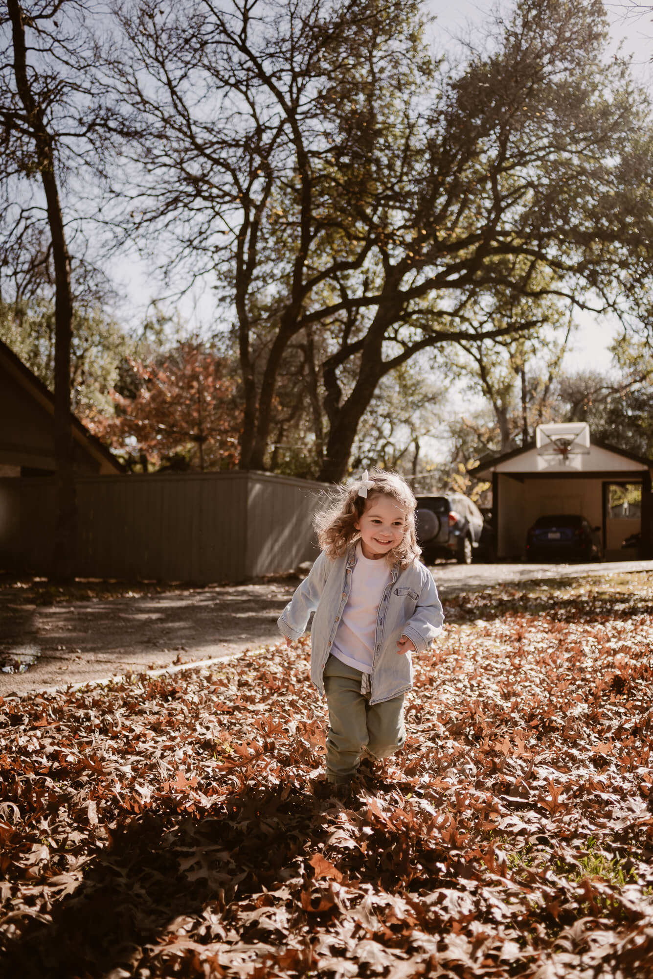 toddler playing outside in the front yard in leaves during an at home family photoshoot in austin texas