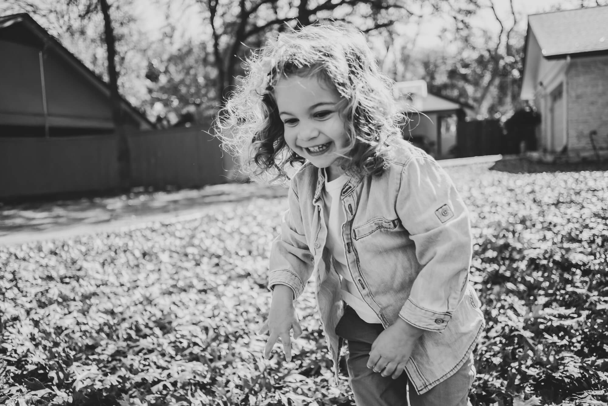 toddler playing outside in the front yard in leaves during an at home family photoshoot in austin texas