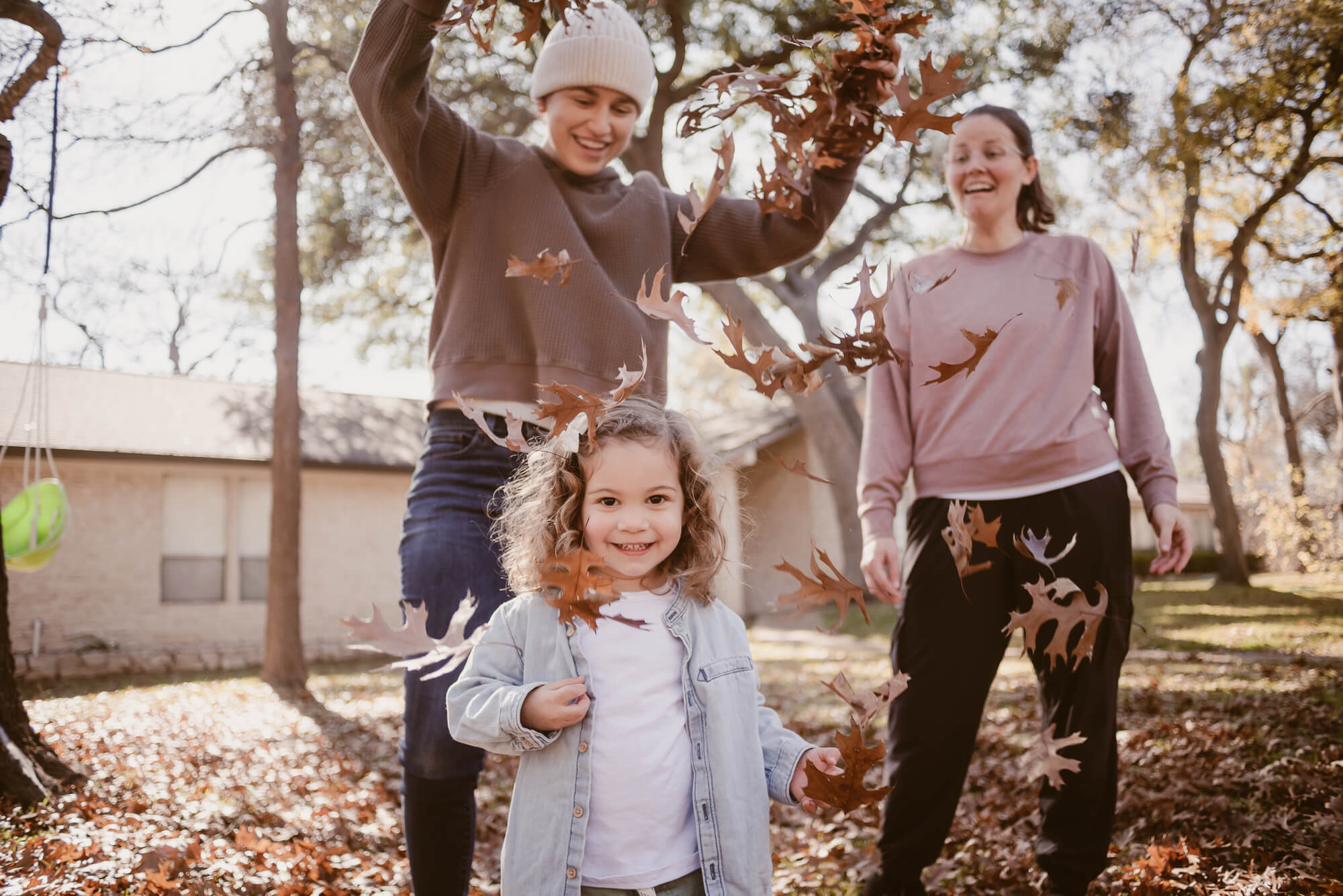 parents dropping leaves on their toddler during an at home family photoshoot in austin texas