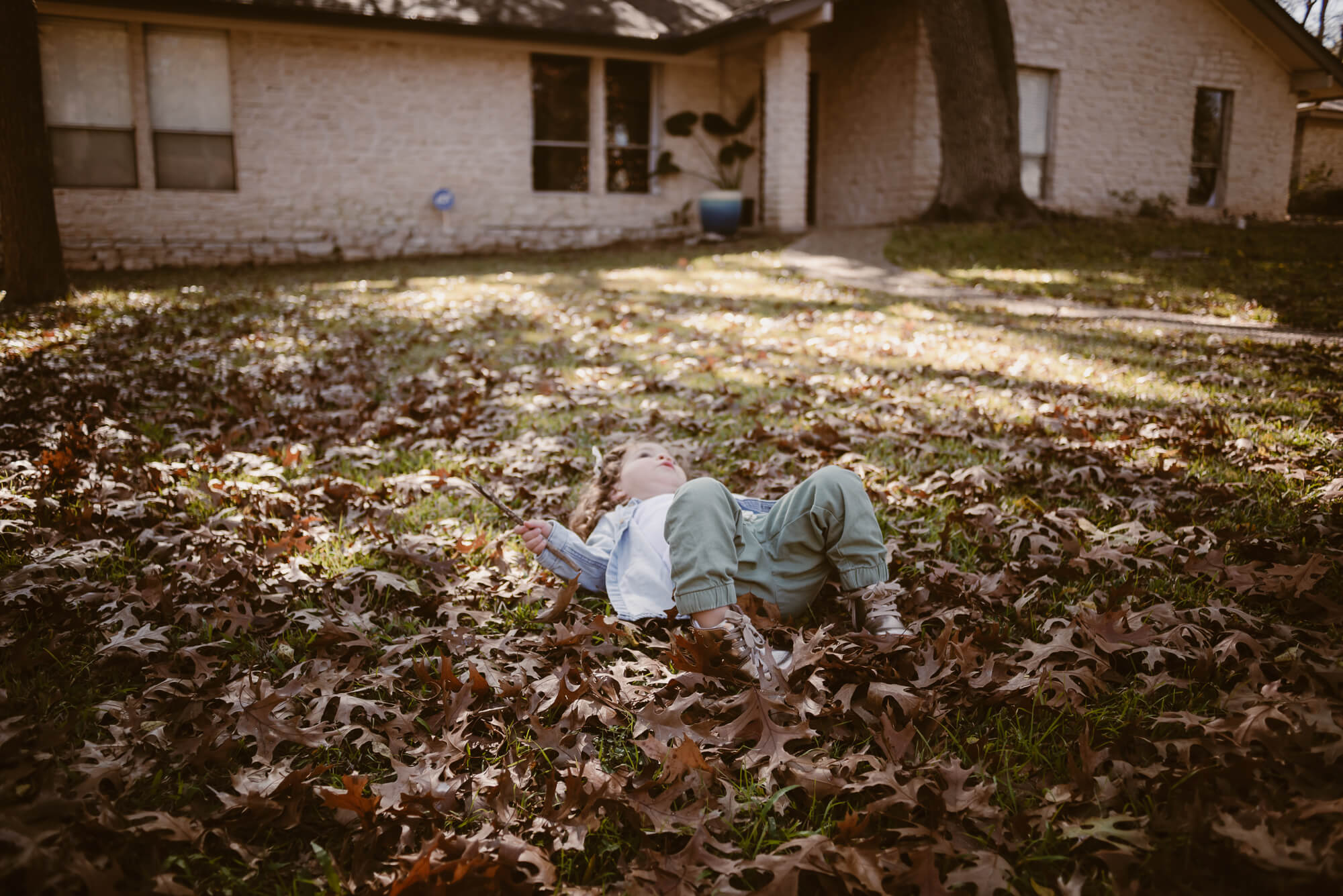Toddler playing in a pile of leaves in the front yard during an at-home family photoshoot in Austin