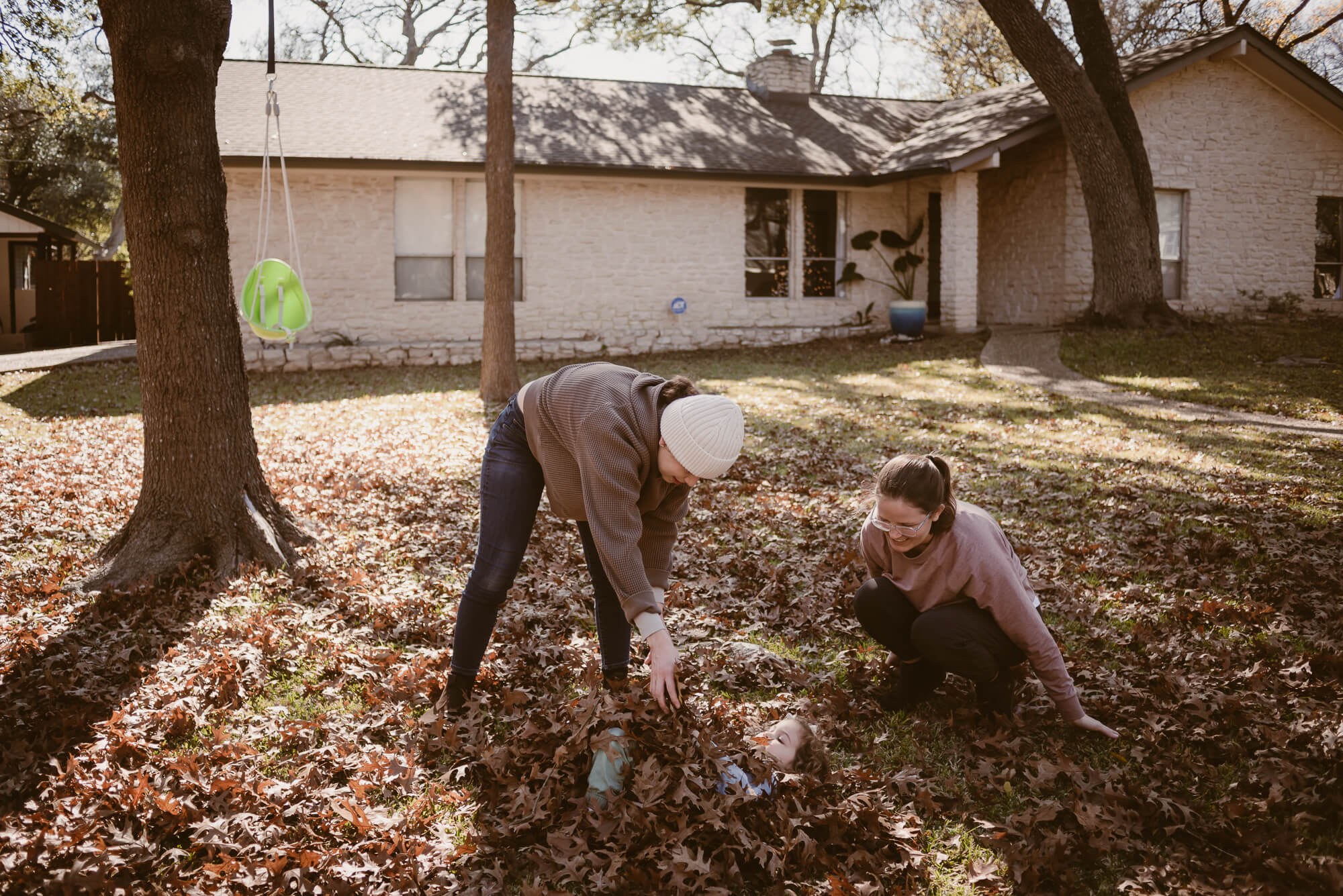 parents burying their toddler in a pile of leaves during an at home family photoshoot in austin texas