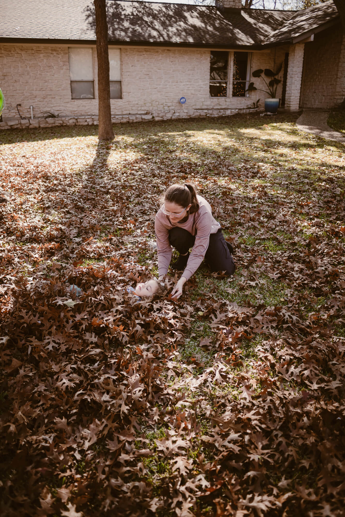 parents burying their toddler in a pile of leaves during an at home family photoshoot in austin texas